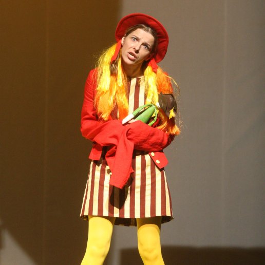 Agnieszka w peruce z długimi, żółtymi włosami, czerwonym kapeluszu, sukience w paski i żółtych jaskrawych rajstopach.