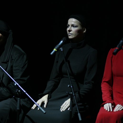 Trzy kobiety siedzą obok siebie. Po środku Agnieszka, w czarnym kostiumie i czarnej chuście na głowie. Zdjęcie oddaje atmosferę milczenia i napięcia.